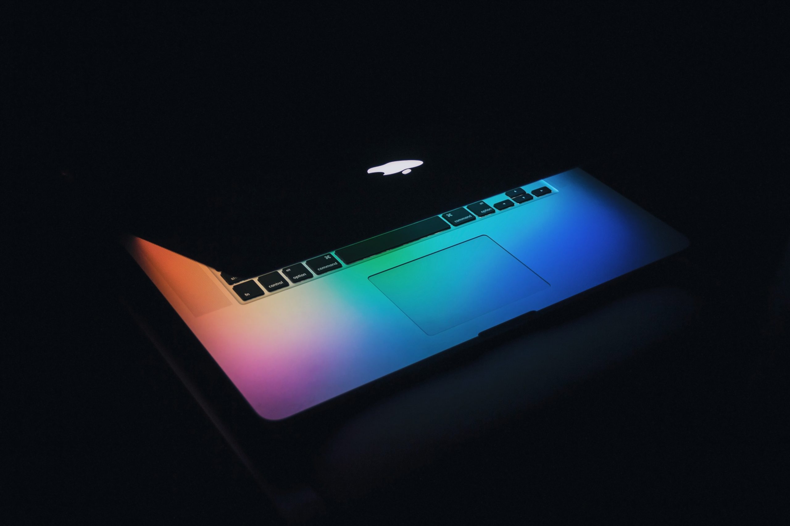 Apple laptop partly open with colorful lights on a black background